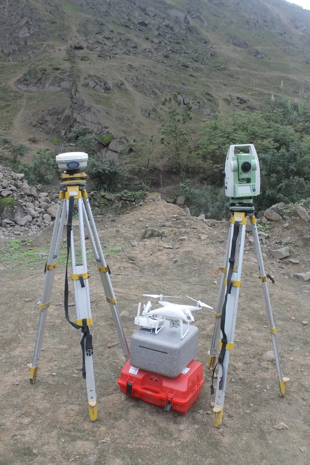 Dos equipos geodésicos sobre trípode junto al maletín de un drone fotogramétrico