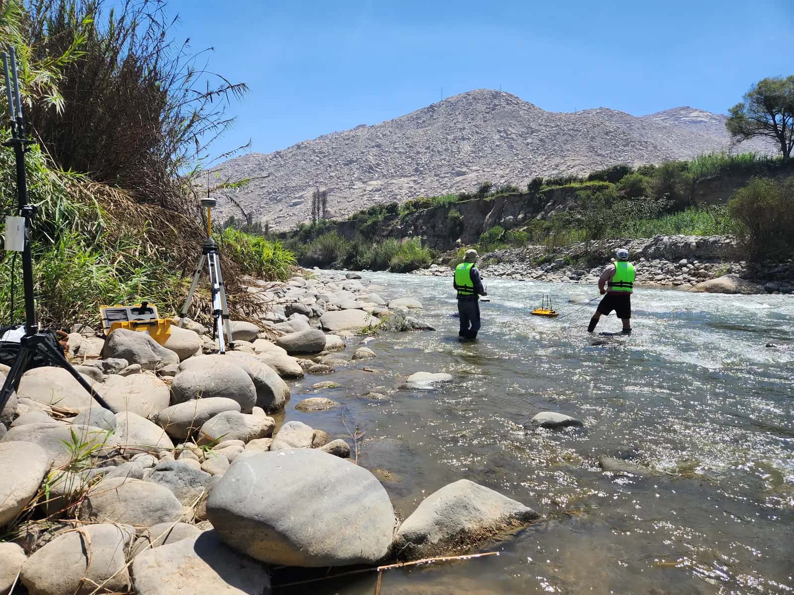 Levantamiento del cauce de un río con la brigada en el agua y la estación de control en la orilla